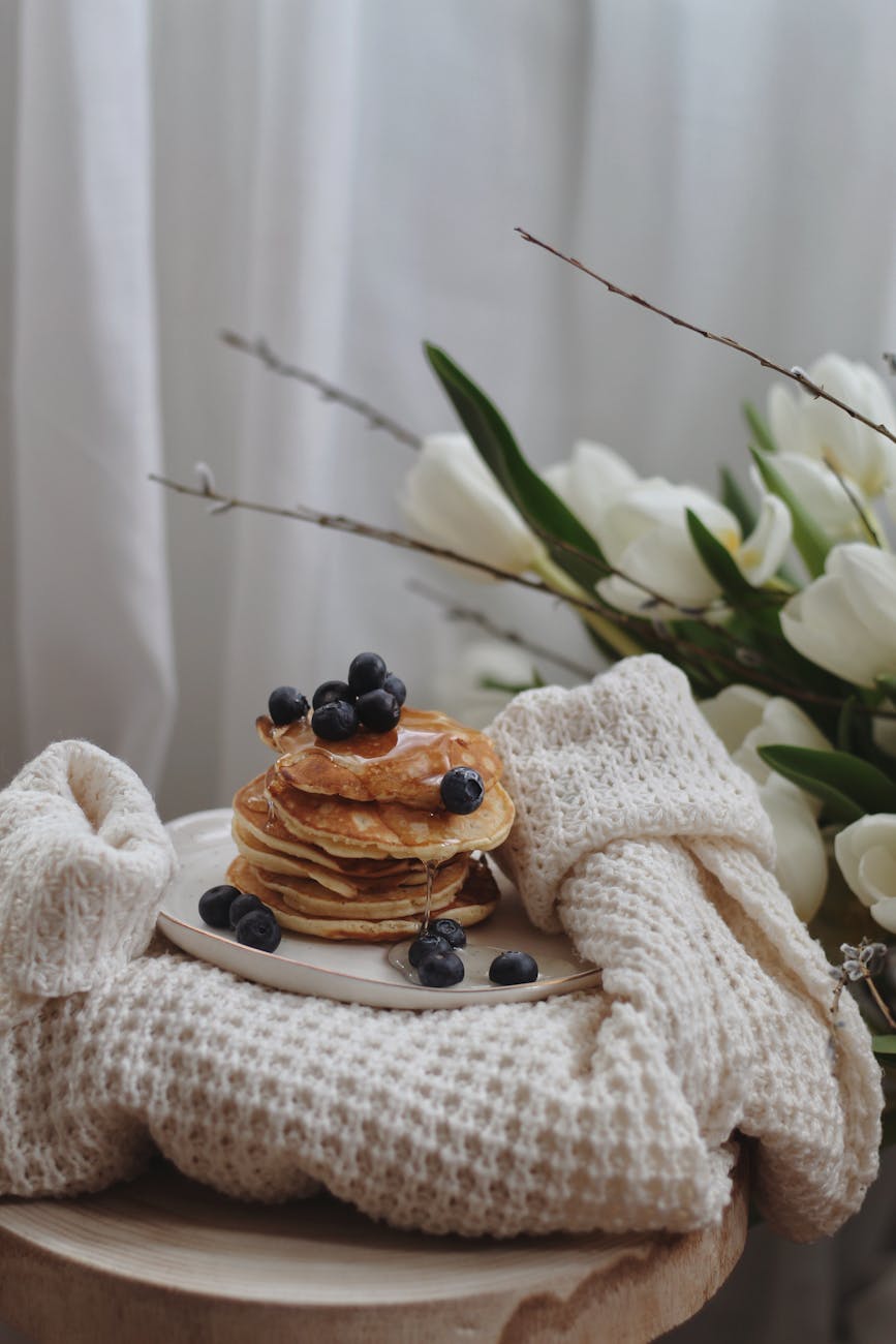 plate of delicious pancakes with berries and maple syrup placed on knitted sweater